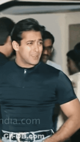 A Man In A Black Shirt Is Standing In A Crowd With India.com Written On The Bottom Left GIF