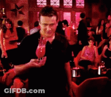 A Man In A Black Shirt Is Standing In A Crowded Restaurant Holding A Glass Of Wine GIF