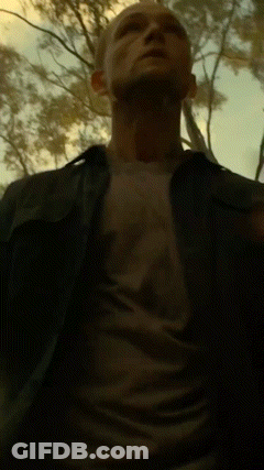 A Man In A Black Shirt Is Standing In A Dark Forest GIF