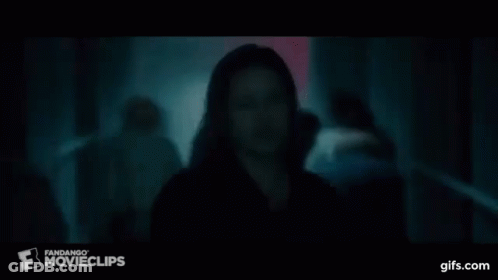 A Man In A Black Shirt Is Standing In A Dark Room In Front Of A Crowd . GIF