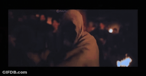 A Man In A Black Shirt Is Standing In A Dark Room With A Blurred Background . GIF
