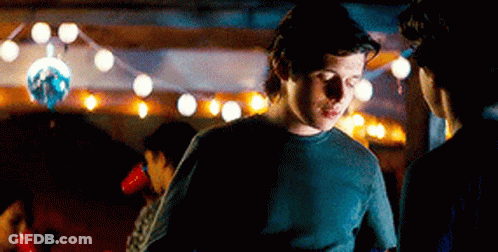 A Man In A Black Shirt Is Standing In A Dark Room With A Disco Ball In The Background . GIF