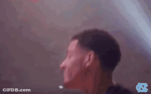 A Man In A Black Shirt Is Standing In A Dark Room With His Hands In The Air . GIF