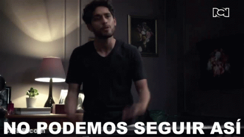 A Man In A Black Shirt Is Standing In A Dark Room With The Words " No Podemos Seguir Así " Behind Him GIF