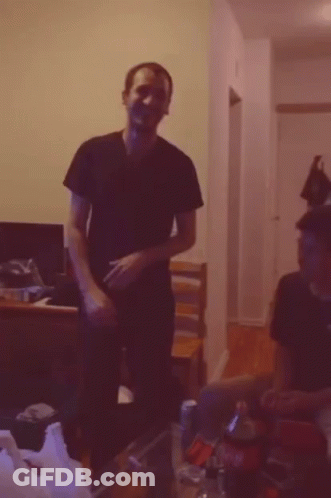 A Man In A Black Shirt Is Standing In A Dark Room GIF