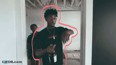 A Man In A Black Shirt Is Standing In A Doorway Holding A Bottle Of Wine . GIF