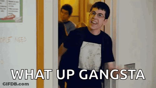 A Man In A Black Shirt Is Standing In A Doorway With The Words `` What Up Gangsta '' Written On The Bottom . GIF