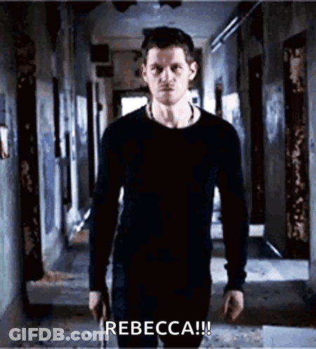 A Man In A Black Shirt Is Standing In A Hallway Holding A Gun And Says Rebecca ! GIF