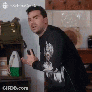 A Man In A Black Shirt Is Standing In A Kitchen Holding A Cell Phone In His Hand . GIF