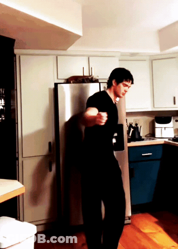 A Man In A Black Shirt Is Standing In A Kitchen Near A Stainless Steel Refrigerator GIF