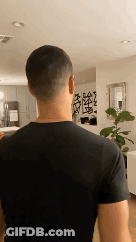 A Man In A Black Shirt Is Standing In A Room GIF