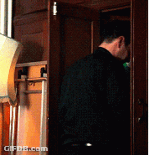 A Man In A Black Shirt Is Standing In A Room GIF
