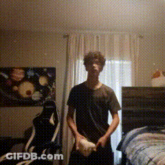 A Man In A Black Shirt Is Standing In A Room With A Painting On The Wall . GIF