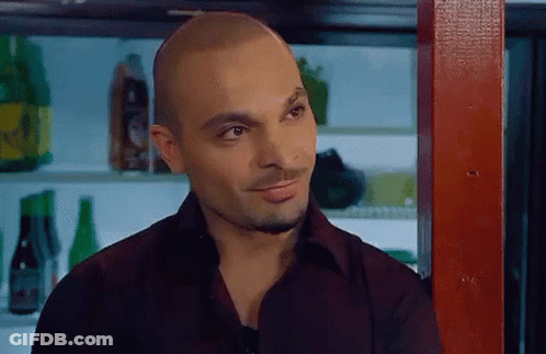 A Man In A Black Shirt Is Standing In Front Of A Bar With Bottles Of Beer On The Shelves . GIF