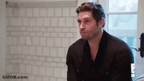 A Man In A Black Shirt Is Standing In Front Of A Bathroom Mirror . GIF