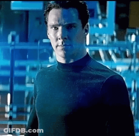 A Man In A Black Shirt Is Standing In Front Of A Blue Wall . GIF