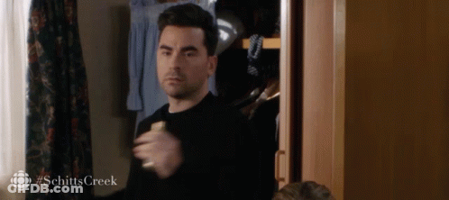 A Man In A Black Shirt Is Standing In Front Of A Closet With #Schittscreek Written On The Bottom GIF