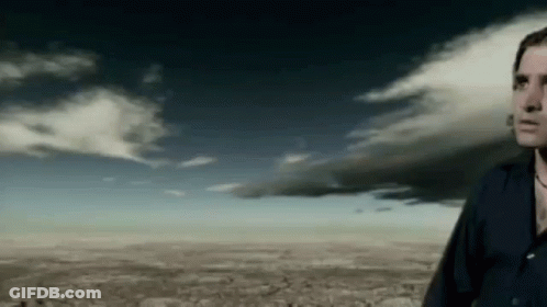 A Man In A Black Shirt Is Standing In Front Of A Cloudy Sky GIF