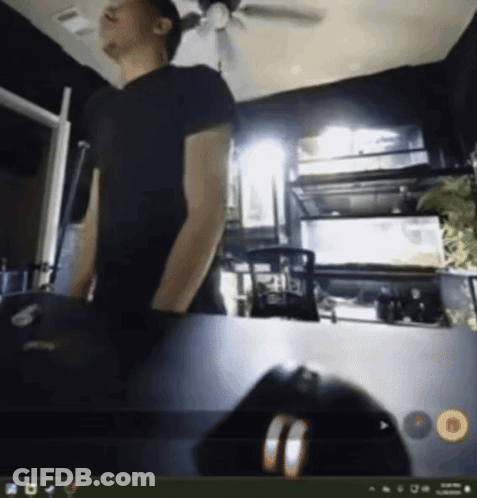 A Man In A Black Shirt Is Standing In Front Of A Computer Monitor GIF