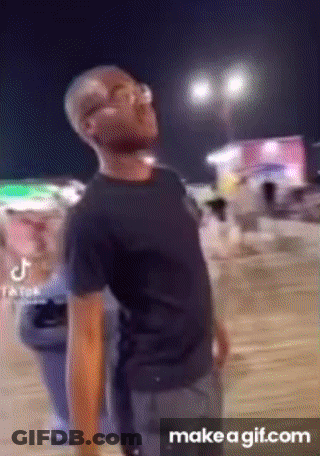 A Man In A Black Shirt Is Standing In Front Of A Crowd Of People At Night . GIF
