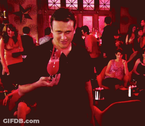 A Man In A Black Shirt Is Standing In Front Of A Crowd Of People GIF