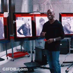 A Man In A Black Shirt Is Standing In Front Of A Display Of Pictures GIF