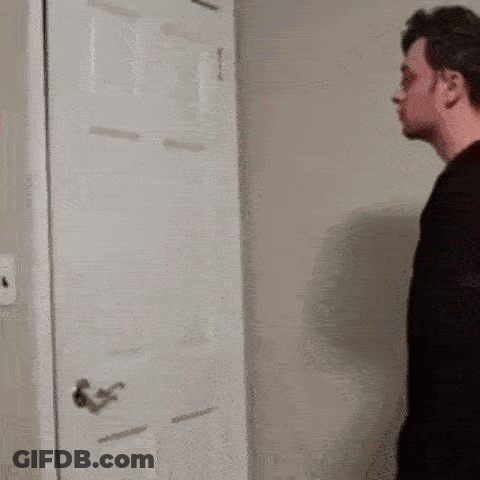 A Man In A Black Shirt Is Standing In Front Of A Door . GIF