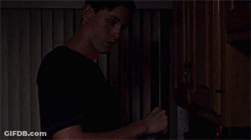 A Man In A Black Shirt Is Standing In Front Of A Fireplace . GIF