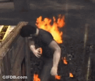 A Man In A Black Shirt Is Standing In Front Of A Large Fire . GIF