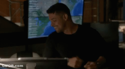 A Man In A Black Shirt Is Standing In Front Of A Large Monitor . GIF