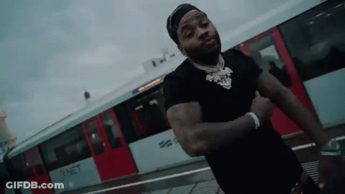 A Man In A Black Shirt Is Standing In Front Of A Red Train . GIF