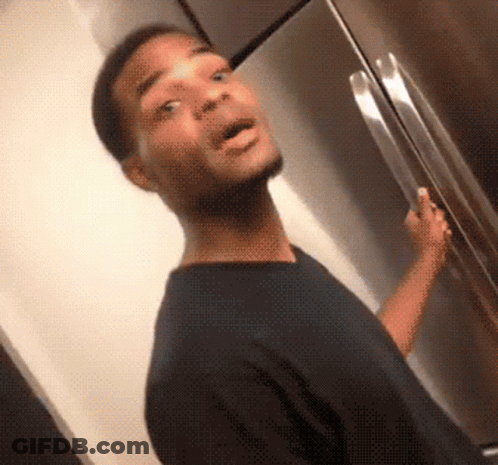 A Man In A Black Shirt Is Standing In Front Of A Refrigerator With His Mouth Open GIF