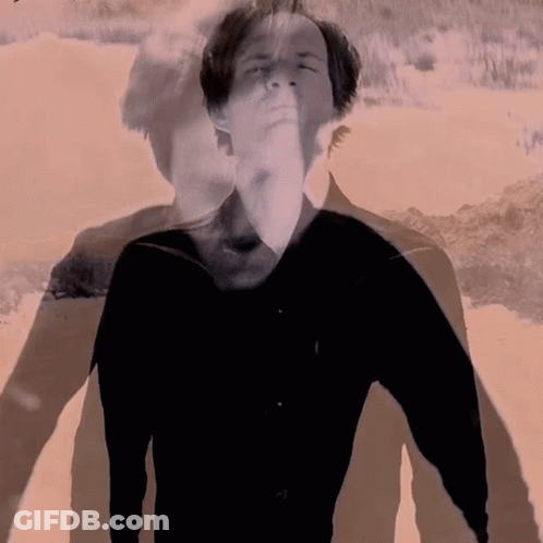 A Man In A Black Shirt Is Standing In Front Of A Sandy Beach GIF