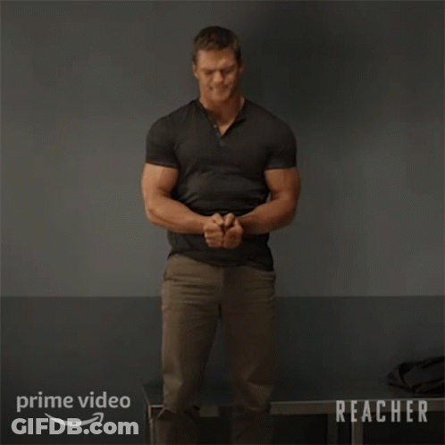 A Man In A Black Shirt Is Standing In Front Of A Sign That Says Prime Video Reacher GIF