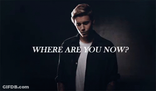 A Man In A Black Shirt Is Standing In Front Of A Sign That Says Where Are You Now GIF