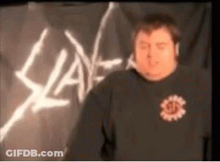 A Man In A Black Shirt Is Standing In Front Of A Slayer Sign . GIF
