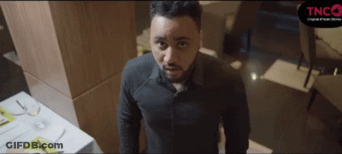 A Man In A Black Shirt Is Standing In Front Of A Table With A Sign That Says Tnco On It GIF