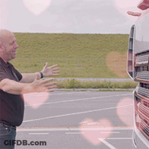 A Man In A Black Shirt Is Standing In Front Of A Truck With His Arms Outstretched GIF