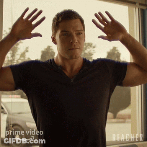 A Man In A Black Shirt Is Standing In Front Of A Window With Reacher Written On It GIF
