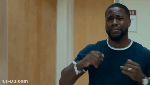 A Man In A Black Shirt Is Standing In Front Of A Wooden Door And Making A Funny Face . GIF