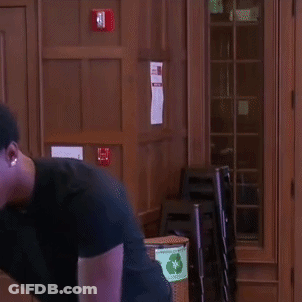 A Man In A Black Shirt Is Standing In Front Of A Wooden Door And Smiling . GIF
