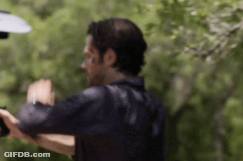 A Man In A Black Shirt Is Standing In Front Of Trees And A Lamp . GIF