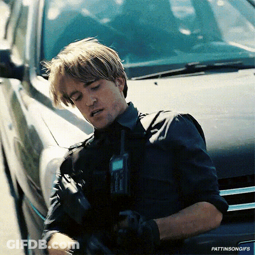 A Man In A Black Shirt Is Standing Next To A Black Car Holding A Walkie Talkie GIF