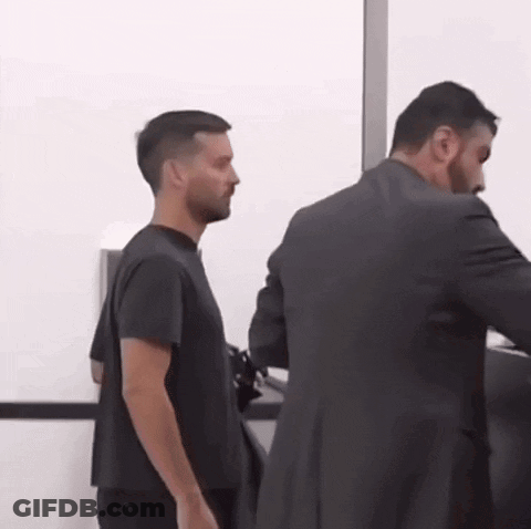 A Man In A Black Shirt Is Standing Next To A Man In A Suit GIF
