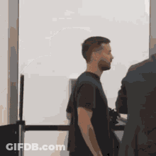 A Man In A Black Shirt Is Standing Next To A Man In A Suit GIF