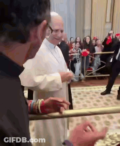 A Man In A Black Shirt Is Standing Next To A Man In A White Robe And Talking To Him . GIF