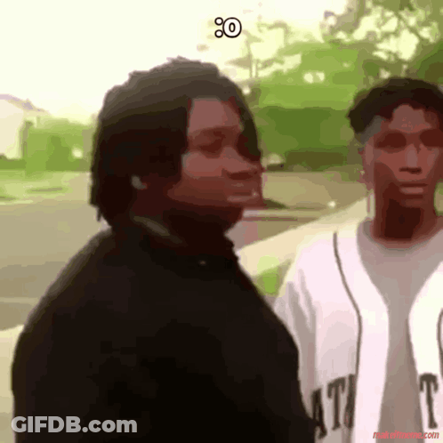 A Man In A Black Shirt Is Standing Next To A Woman In A White Shirt That Says T. GIF