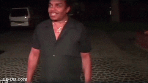 A Man In A Black Shirt Is Standing On A Cobblestone Road GIF