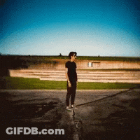 A Man In A Black Shirt Is Standing On A Sidewalk GIF