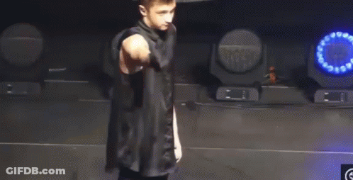 A Man In A Black Shirt Is Standing On A Stage With A Microphone In His Hand . GIF